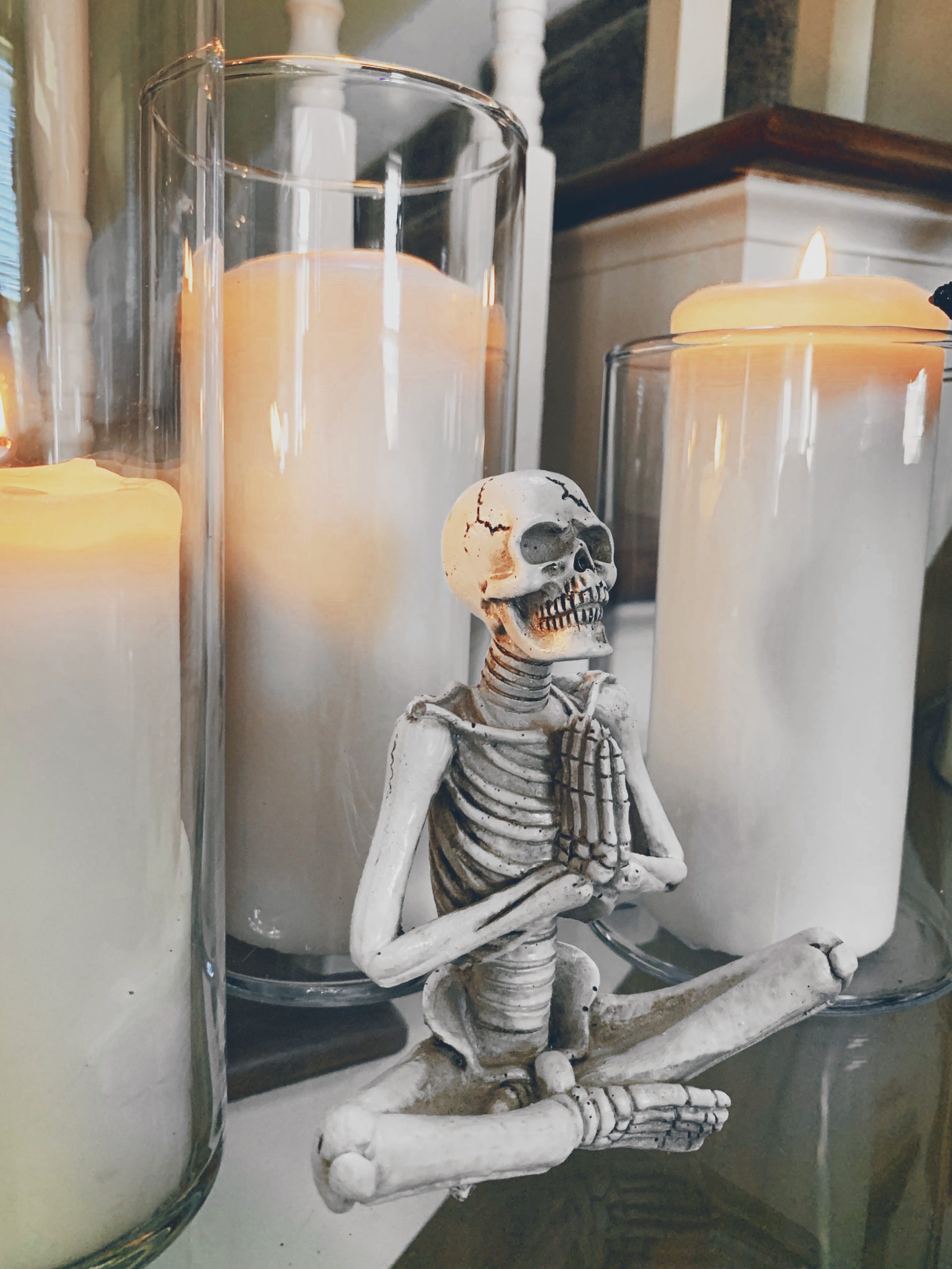 chic halloween decor, halloween skeleton doing namaste pose in front of pillar candles