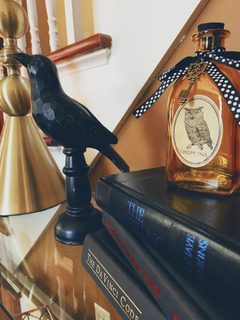 chic halloween decor, wooden black raven sitting on a gold console table next to a stack of black books