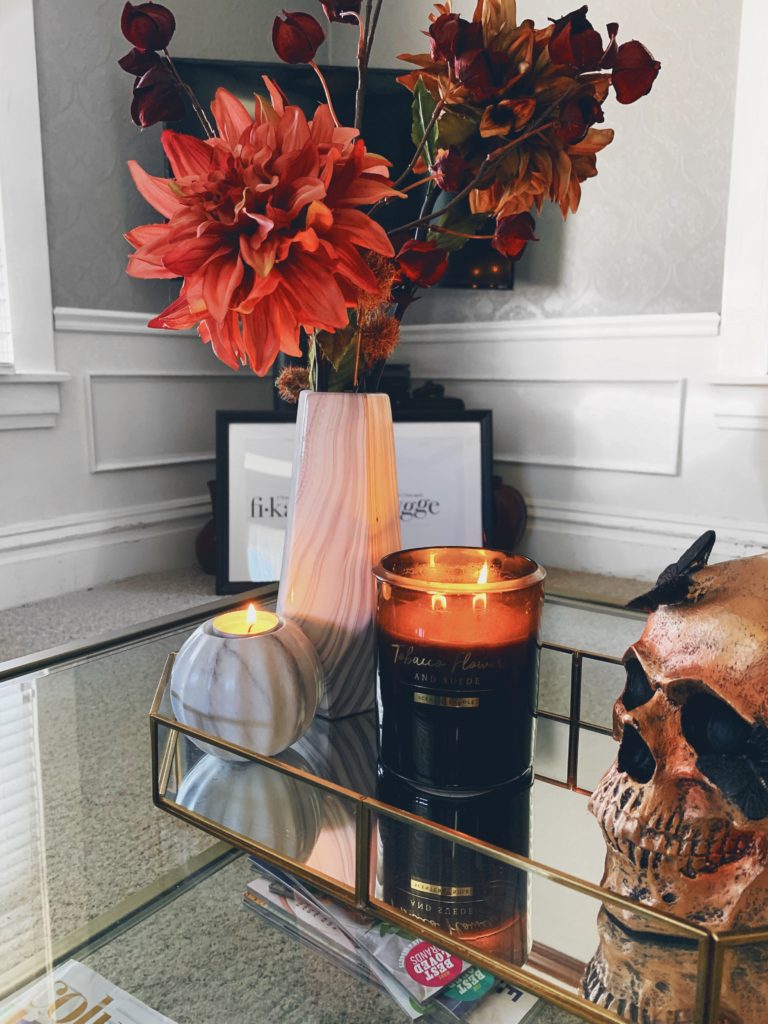 chic halloween decor, fall flowers sitting on a coffee table next to a black candle and a booze skull