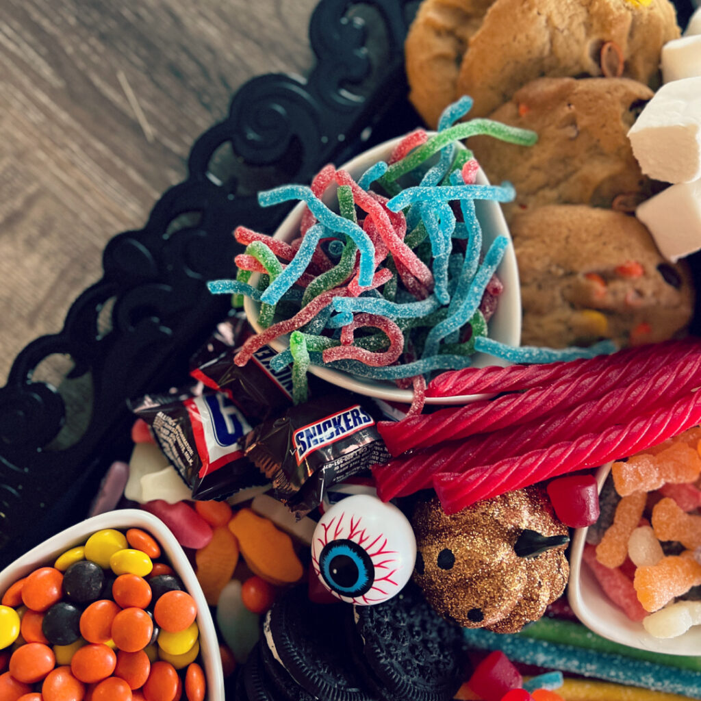 Halloween candy charcuterie board with a mix of sour and chocolate candies and fake spiders, bats and pumpkins as decoration.