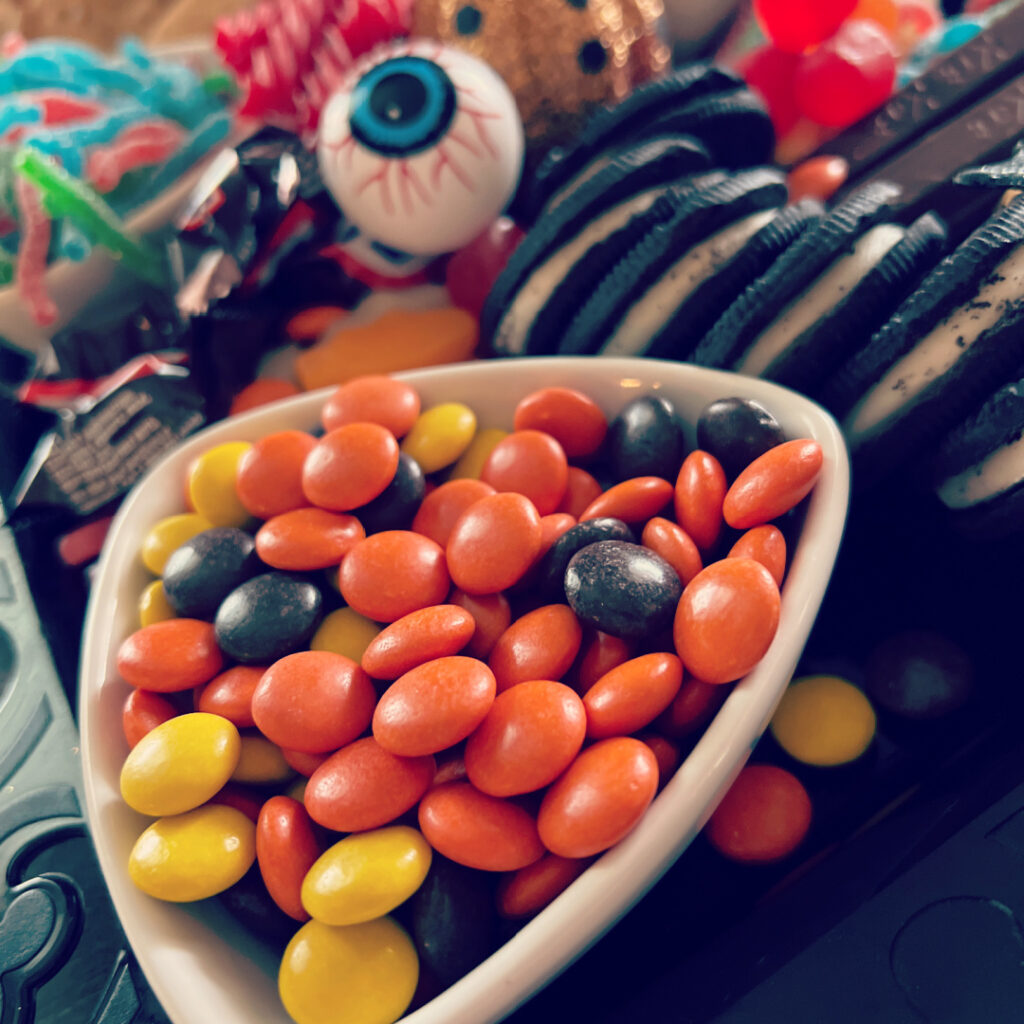 Halloween candy charcuterie board with a mix of sour and chocolate candies and fake spiders, bats and pumpkins as decoration.