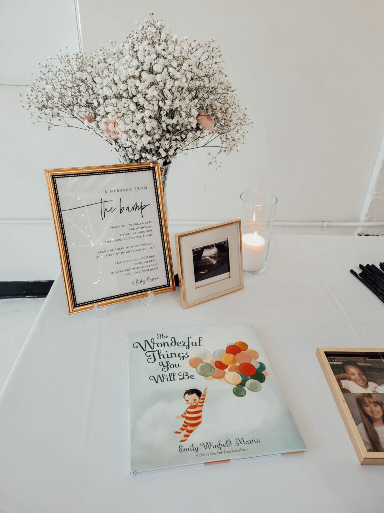 Welcome sign and table with a kids book and a big vase of flowers for a cloud themed baby shower