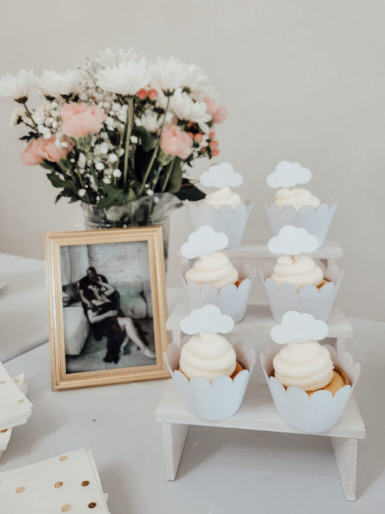 white cloud cupcakes on a white cupcake stand on a dessert table at a cloud themed baby shower