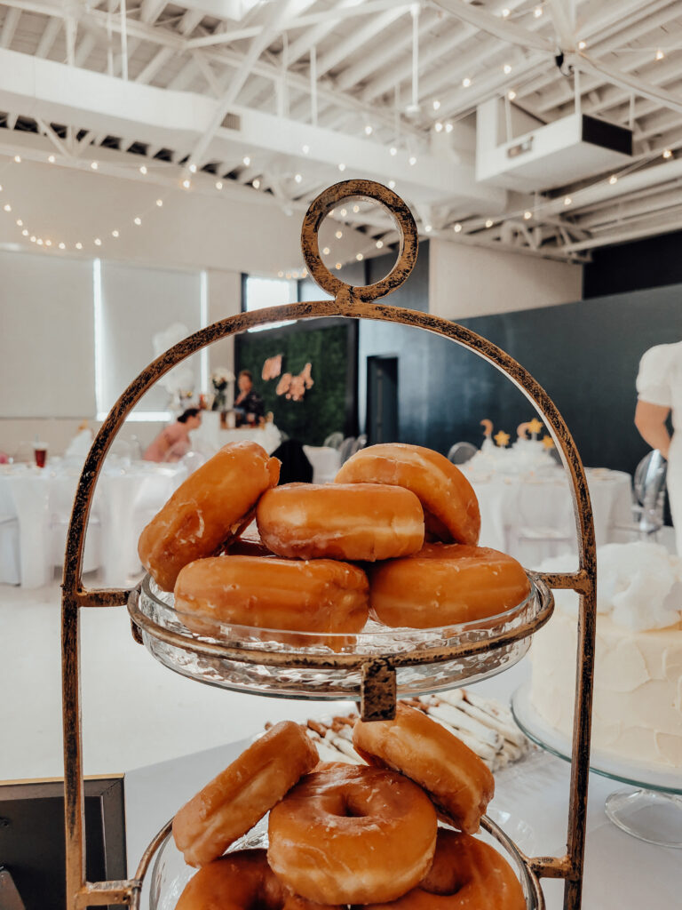 A food tier with glazed donuts on it setting on a dessert table at a cloud themed baby shower