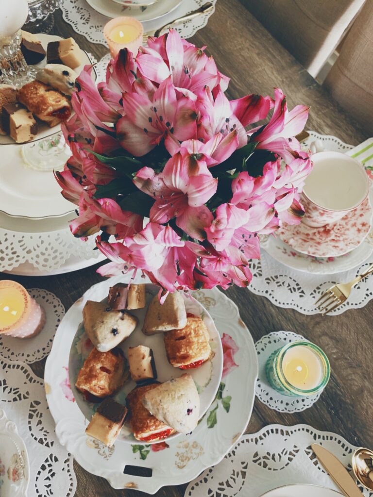 beautiful purple flowers in a vase on a table with a tray of scones and other tea party finger foods