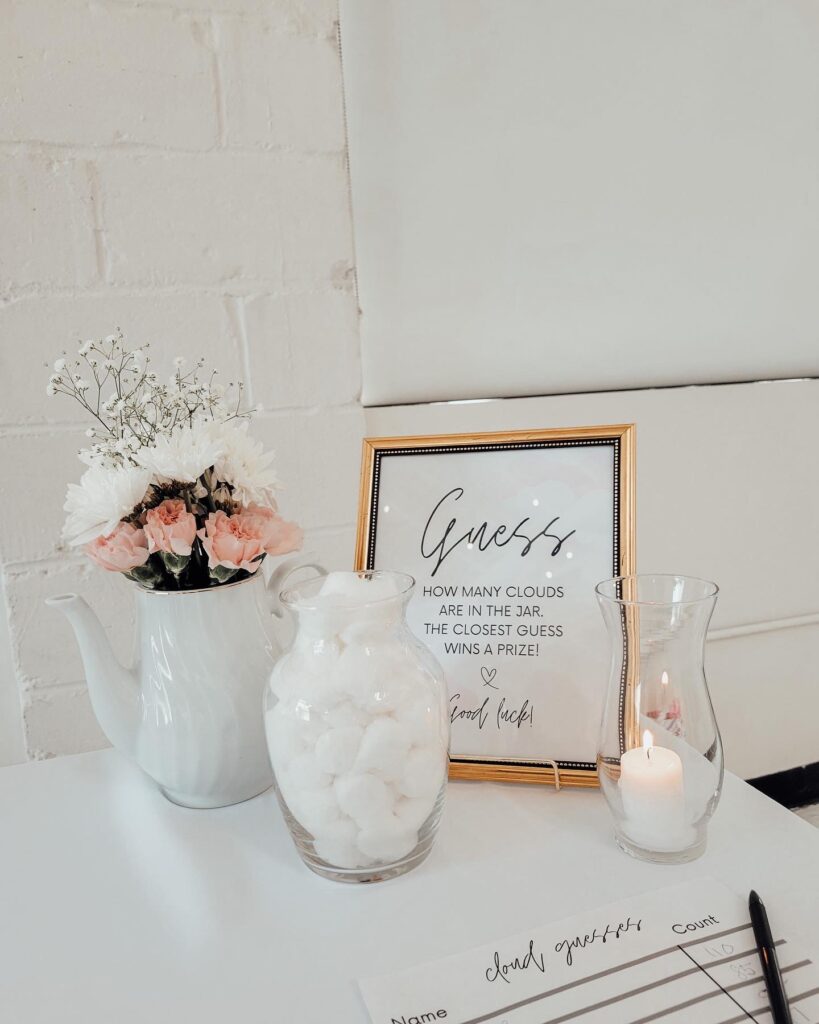 white flower vase with pink and white flowers in it with a guessing game for a cloud themed baby shower