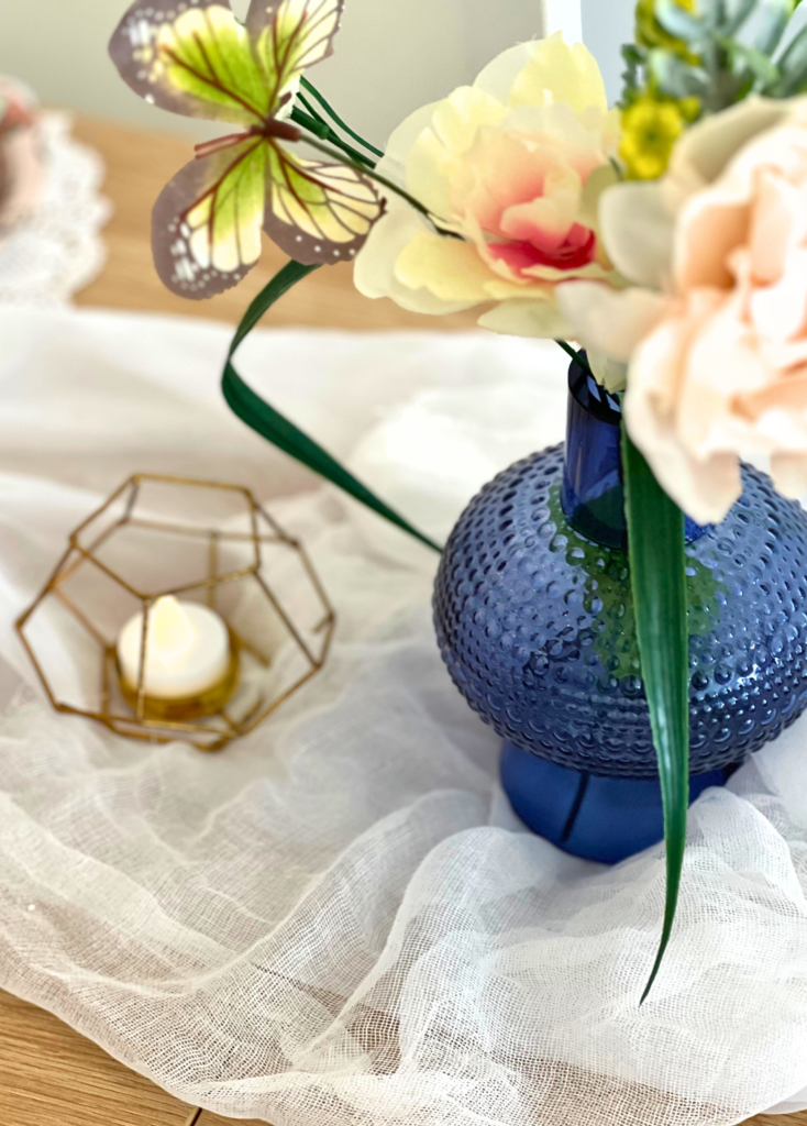 blue vase with faux flowers sitting on a table linen for a garden party themed birthday