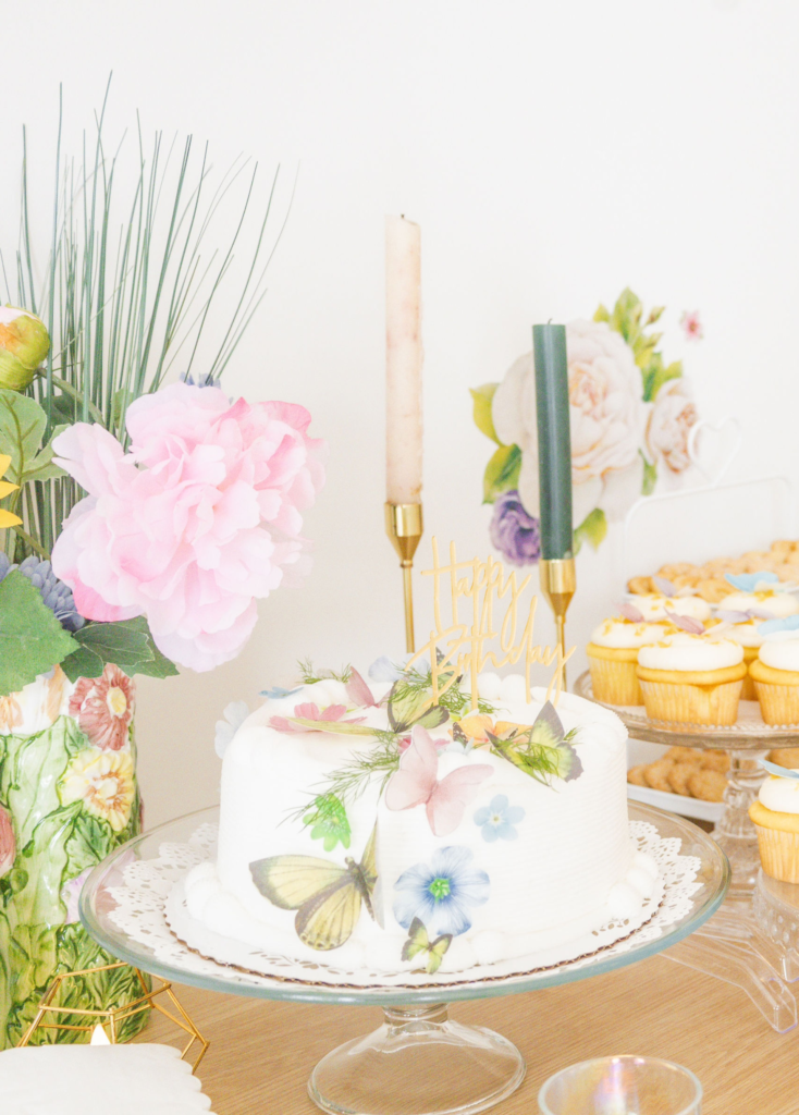 A beautiful white cake on a dessert table at a garden party themed birthday party