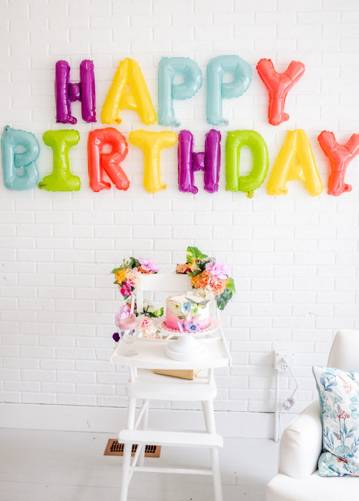 White highchair decorated in florals with a colorful happy birthday balloon display behind it for a garden party themed birthday party