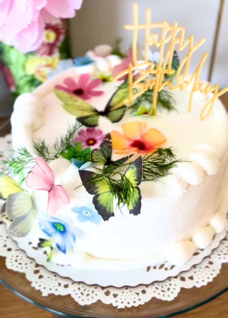 White cake with sugared faux butterflies and a happy birthday cake topper for a garden party