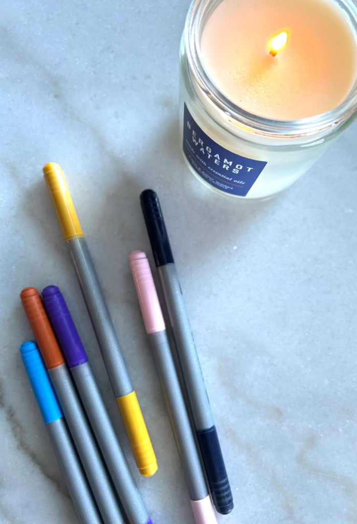 colorful pens sitting next to a candle for a blog post about productivity and organization hacks for working moms