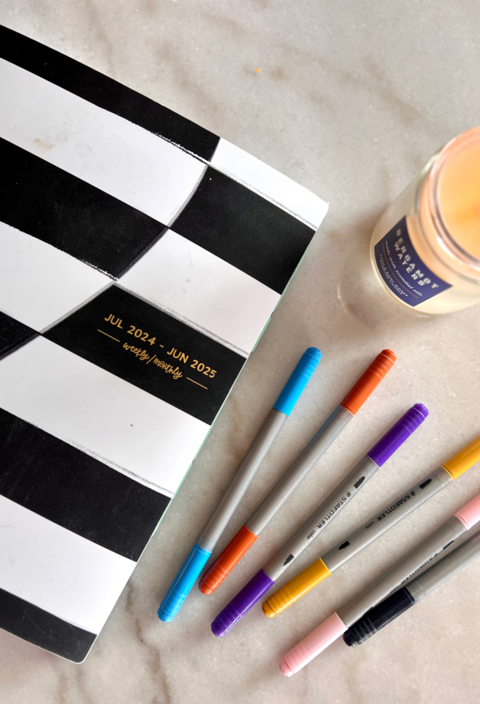 black and white planner sitting next to colorful pens in a blog post about productivity and organization hacks for working moms