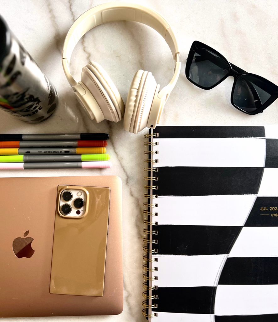 flat lay of planner, laptop, headphones and sunglasses