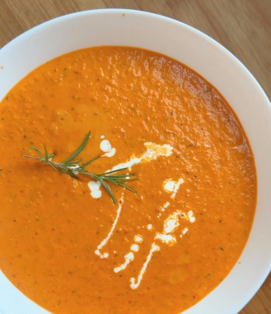 creamy roasted tomato soup in a white bowl with a rosemary sprig on top