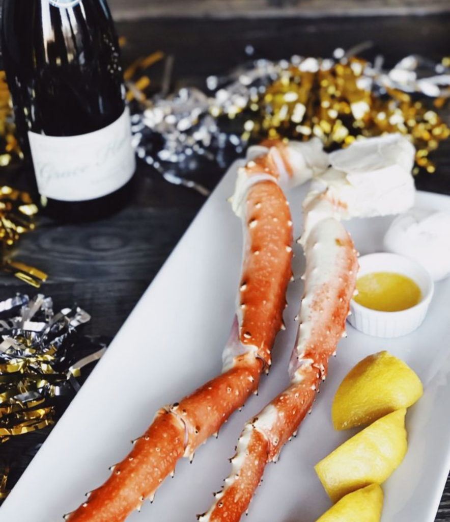 Crab leg with drawn butter sitting on a dinner table with festive NYE decor around it for a NYE celebration at home