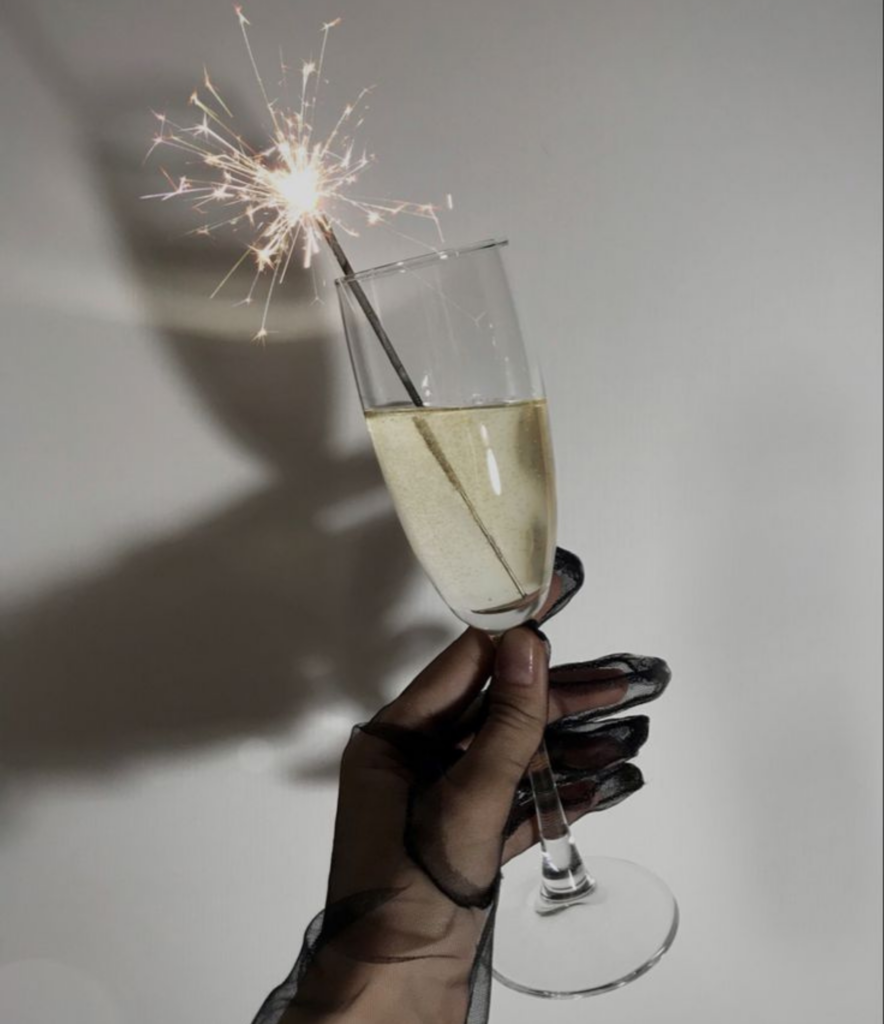 holding a glass of champagne with sparkler and black gloves on for an aesthetic NYE celebration at home