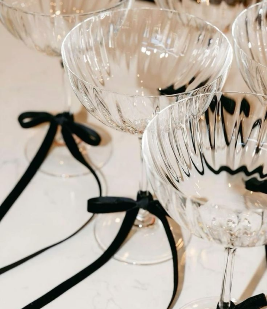 Festive champagne coupe glasses with a black ribbon tied on the stem for a NYE celebration at home