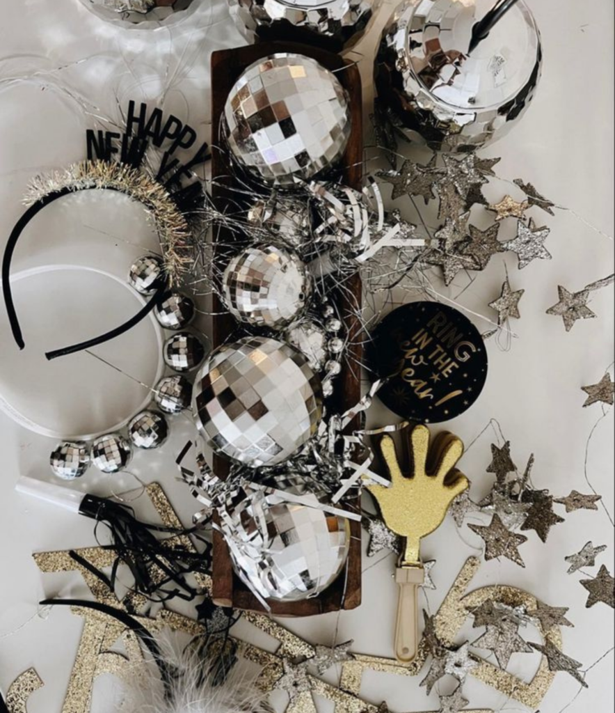 A New Years eve flatlay image with disco balls, festive headbands and clappers, all items for a festive NYE celebration at home