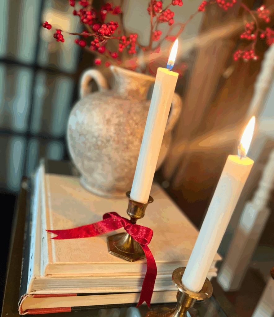 brass candle sticks with burgundy bows tied around them with a bunch of holly berries behind them for a blog post about the Ralph Lauren Christmas trend.