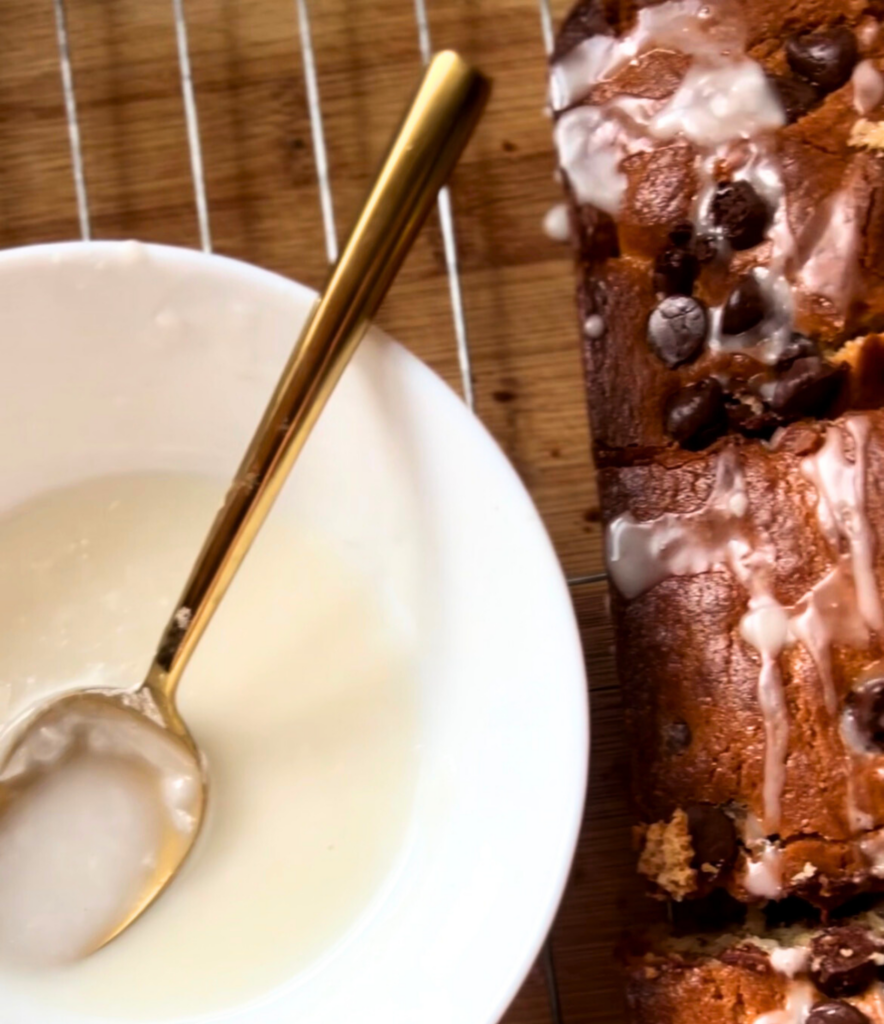 Drizzling vanilla glaze over freshly baked chocolate chip cookie cake
