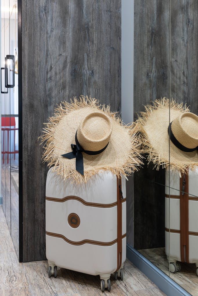 A chic straw hat resting on a suitcase in a contemporary hotel hallway, ready for travel.