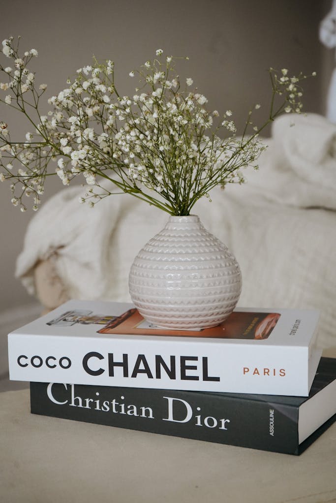 Elegant scene featuring a vase with white flowers atop Chanel and Dior books.
