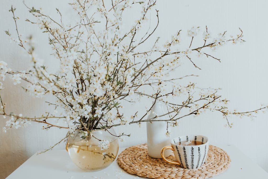 Minimalist decor with blossoming branches and a decorative porcelain cup on a woven mat.
